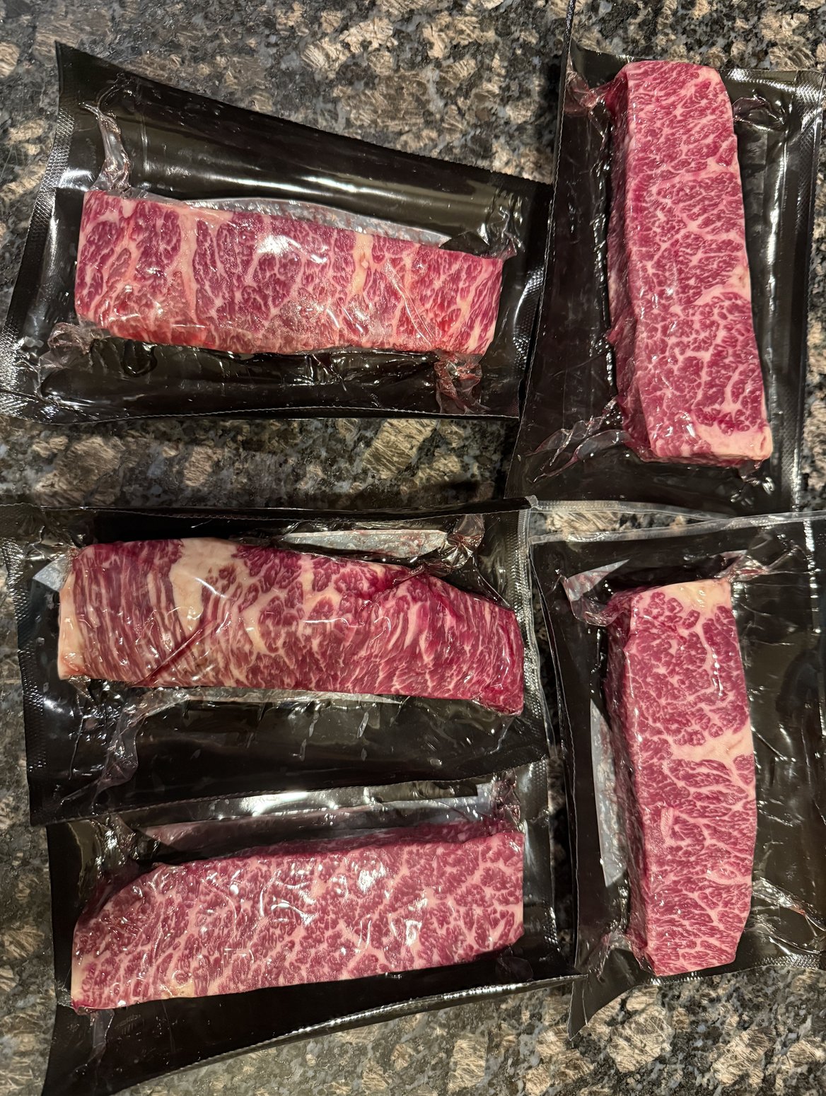Five vacuum-sealed marbled Wagyu Denver steaks on granite